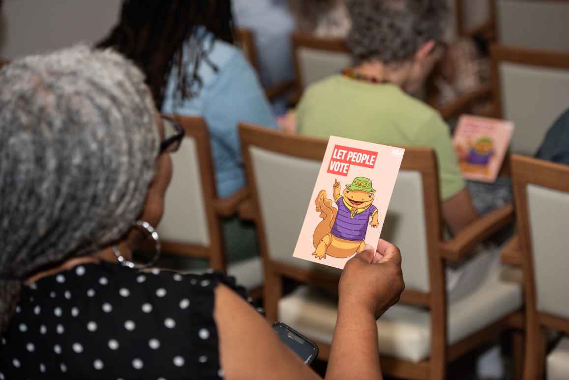 Woman holding placard of an animated salamander holding a sign that says "Let People Vote"